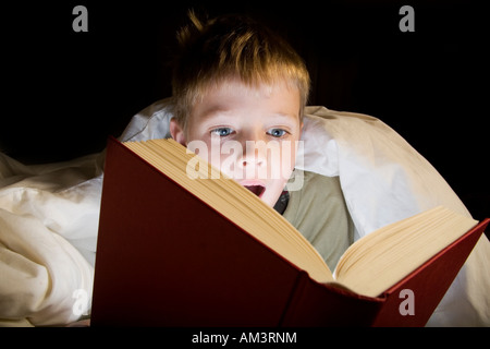 Junge liest unter der Bettdecke bei Fackelschein Stockfoto