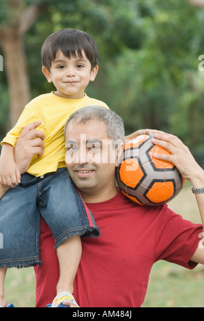Porträt eines Mitte erwachsenen Mannes tragen seinen Sohn auf seine Schulter und halten einen Fußball Stockfoto