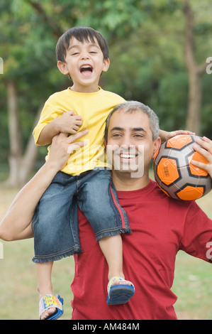 Mitte erwachsenen Mannes tragen seinen Sohn auf seine Schulter und halten einen Fußball Stockfoto