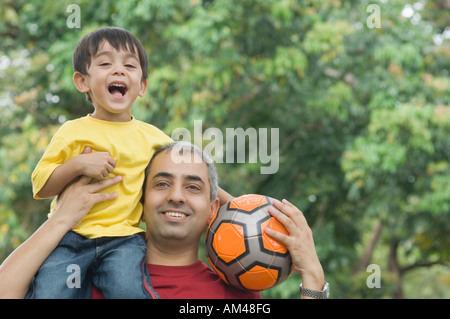 Nahaufnahme eines Mitte erwachsenen Mannes tragen seinen Sohn auf seine Schulter und halten einen Fußball Stockfoto