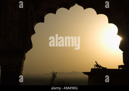 Silhouette einer Kanone, betrachtet durch einen Bogen bei Sonnenuntergang, Neemrana Fort, Neemrana, Alwar Rajasthan, Indien Stockfoto