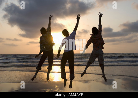 Rückansicht der drei jungen Männer springen mit ihren Händen angehoben am Strand Stockfoto