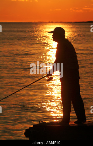 Fischer auf einem Dock bei Sonnenuntergang mit seinem Spin Casting Pol Stockfoto