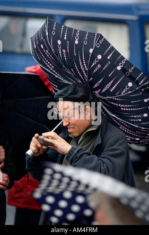 Der Wind bläst einen brolly innen heraus, während dieser Mann die Bilder auf seiner Digitalkamera prüft. Bild von Jim Holden. Stockfoto