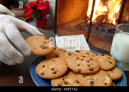 Während Santa Claus Blätter präsentiert sich in einem Haus, greift er nach einen Schokoladenkeks Links für ihn zusammen mit einem Glas Milch. Stockfoto