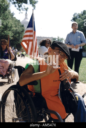 Frau mit einer Behinderung, die einen Rollstuhl für die Mobilität der amerikanischen Flagge und gibt die Handzeichen für den Frieden nutzt. Stockfoto