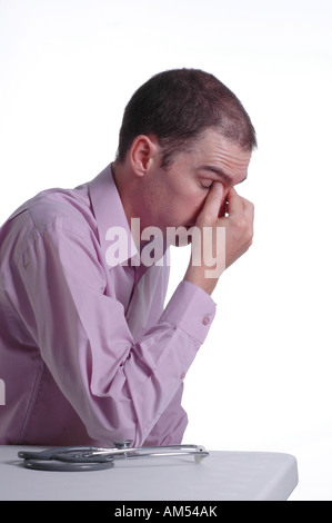 Ein junger männlicher Arzt an seinem Schreibtisch reibt seine Augen mit Müdigkeit aus lange Arbeitszeiten Stockfoto