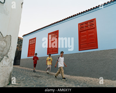 Junge Kinder zu Fuß in einer Gasse eine bunt bemalte Wand mit roten Fenstern auf La Gomera Kanarische Inseln Stockfoto