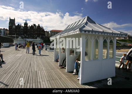 Touristen sitzen in traditionellen hölzernen Unterständen auf Cromer Pier, Norfolk Küste North East Anglis England UK GB Großbritannien Stockfoto