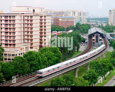 Ein Zug bewegt sich weg von einer Station unter öffentlichen Wohnsiedlungen in Singapur The Mass Rapid Transit Stockfoto