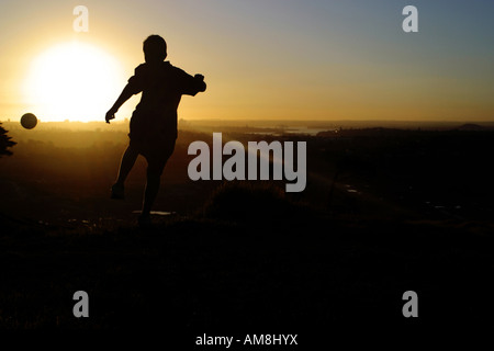 junger Mann treten einen Fußball in den Sonnenuntergang Stockfoto