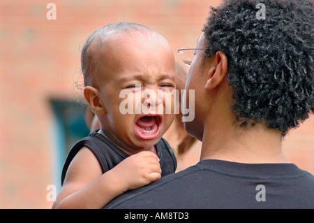 Schreiendes Baby Hilfe von Dad mit Mutter im Hintergrund Stockfoto