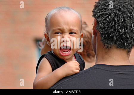 Schreiendes Baby Hilfe von Dad mit Mutter im Hintergrund Stockfoto