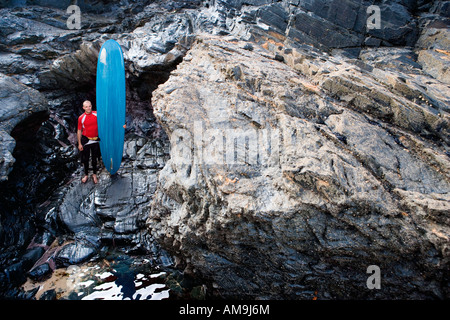 Mann, stehend mit Surfbrett auf den großen Felsen. Stockfoto