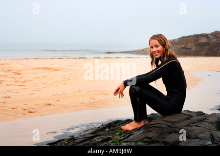 Frau sitzt am Strand in Neoprenanzug lächelnd. Stockfoto