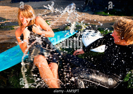 Paar Spritzwasser auf einander lachend mit Surfbrettern im Hintergrund. Stockfoto