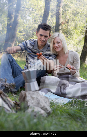 Zu zweit am Campingplatz kochen Hotdogs und lächelnd. Stockfoto