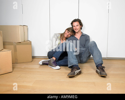 Paar auf Boden lächelnd mit Umzugskartons in der Nähe sitzen. Stockfoto