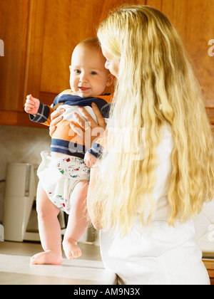 Frau halten Baby bis auf die Küche Zähler lächelnd. Stockfoto