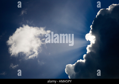 Strahlen des Sonnenlichts, die hinter einer Wolke gegen den blauen Himmel leuchten Stockfoto