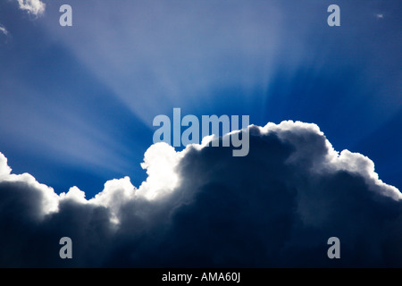 Strahlen des Sonnenlichts, die hinter einer Wolke gegen den blauen Himmel leuchten Stockfoto