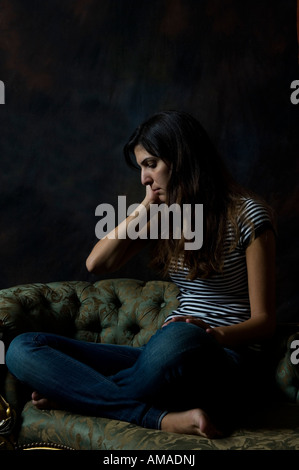 traurige Frau Schneidersitz sitzen auf einem sofa Stockfoto