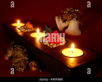 DEKORIERTE Kerzenständer mit drei Kerzen, Weihnachtsglocken und goldenen Tannenzapfen auf dunklem Hintergrund Stockfoto