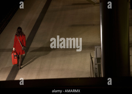 Eine Frau zu Fuß entlang einem Bahnsteig in der Nacht mit einem Koffer Stockfoto