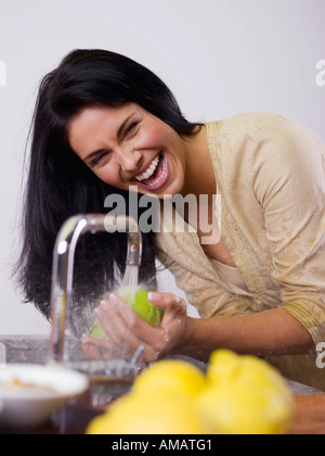 Frau Obst bei Küchenspüle waschen, lachen Stockfoto