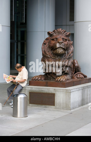 Ein Mann liest seine Zeitung eines der Löwe aus Bronze Statuen vor der HSBC in Hong Kong. Stockfoto