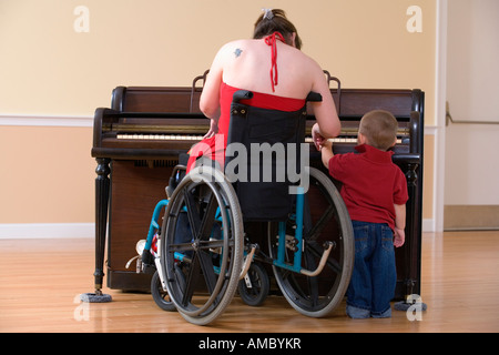 Rückansicht einer Mitte Erwachsene Frau im Rollstuhl, Lehre ein Junge auf das Klavier zu spielen. Stockfoto