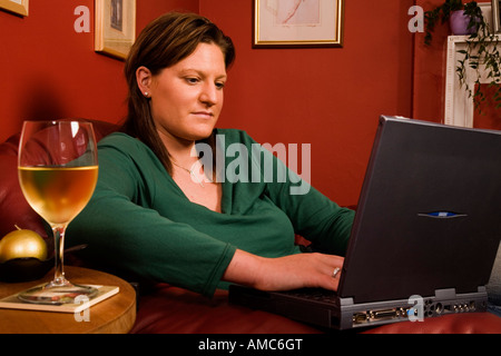 Frau auf einem Laptop bei einem Glas Weißwein Stockfoto