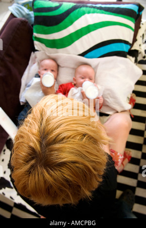 auf der Suche über eine Mütter-Kopf und Schultern, wie sie gleichzeitig Flasche ernährt Zwillingen ihre Milch auf einem sofa Stockfoto