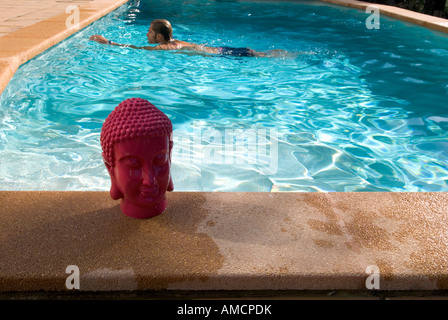 ein Mann schwimmt über einen privaten Pool im Hintergrund mit einem rosa Buddha-Kopf im Vordergrund auf Seite Stockfoto