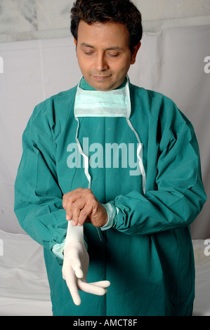 VEP72234 jungen indischen Arzt Chirurg mit Gesichtsmaske und in grün Betrieb Theater Kleid tragen von OP-Handschuhen Stockfoto