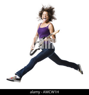 Mädchen mit Zahnspange und Gitarre springen und Zunge heraus Stockfoto