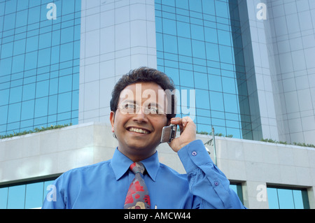 VEP72167 junge indische Executive mit Brille Lächeln und reden über Handy vor modernen Gebäude Stockfoto