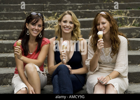 Drei Frauen sitzen auf Schritte im Freien essen Eiscreme-Kegel lächelnd Stockfoto