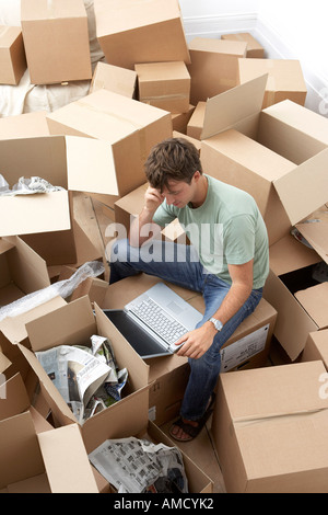 Mann, sitzend unter Umzugskartons mit Laptop-Computer Stockfoto