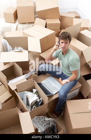 Mann, sitzend unter Umzugskartons mit Laptop-Computer Stockfoto