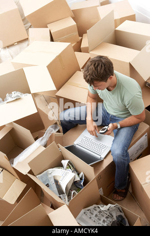 Mann, sitzend unter Umzugskartons mit Laptop und Handy Stockfoto