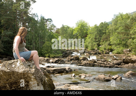Junge Frau sitzt durch die Falls of Dochart in Perthsire Schottland Stockfoto