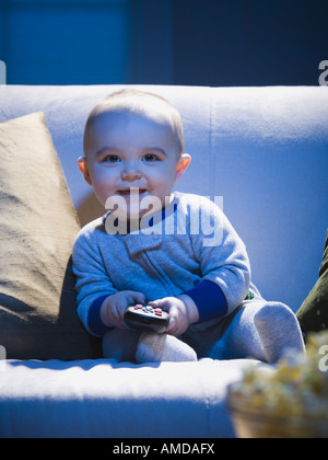 Baby auf Sofa mit TV remote lächelnd Stockfoto