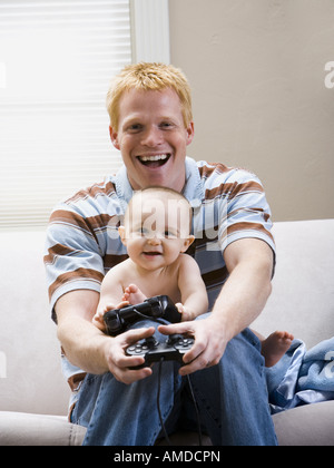 Mann und Baby auf Sofas mit Videospiel-Controller lächelnd Stockfoto