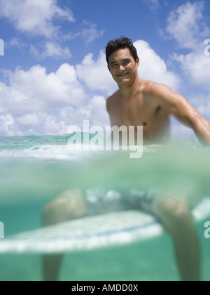 Mann sitzt auf Surfbrett im Wasser lächelnd Stockfoto