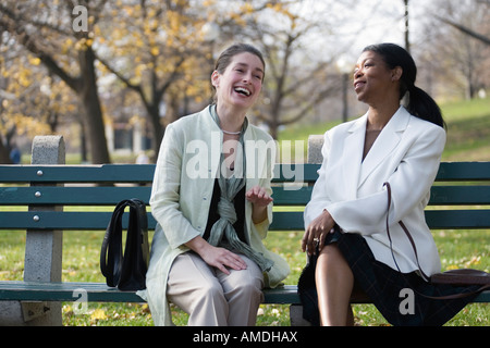 Zwei Frauen sitzen auf einer Bank im Park und lachen. Stockfoto