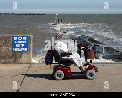 Walton auf der Naze Strandpromenade mit Lady auf einer Behinderung Motorroller aufpassenden Knaben in rauer See Walton pier über Essex England Großbritannien Stockfoto