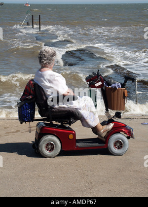 Walton On The Naze Strandpromenade mit Dame auf eine Behinderung motorisierte Roller Blick auf rauer See Stockfoto