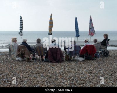 Eine Gruppe von Senioren in einem Tag sitzen zusammen auf Kiesel steinigen Strand im Vorgriff auf etwas Sonne Sonnenschirm bereit oder vielleicht Regen Sussex England Großbritannien Stockfoto
