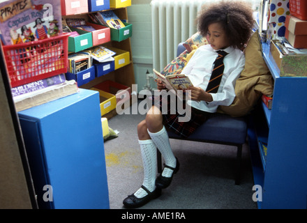 Kleine schwarze Mädchen liest ein Buch einer Schulbibliothek in London. Stockfoto